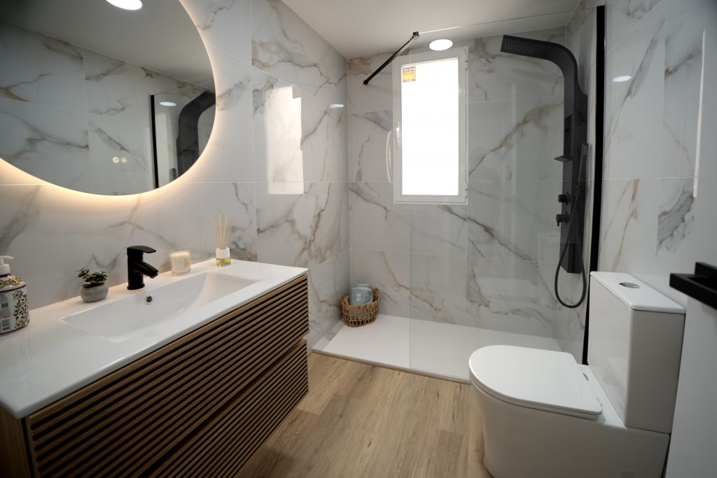 Baño moderno con mármol y espejo LED encendido, fotografía de interiores por Inmofoto360.
